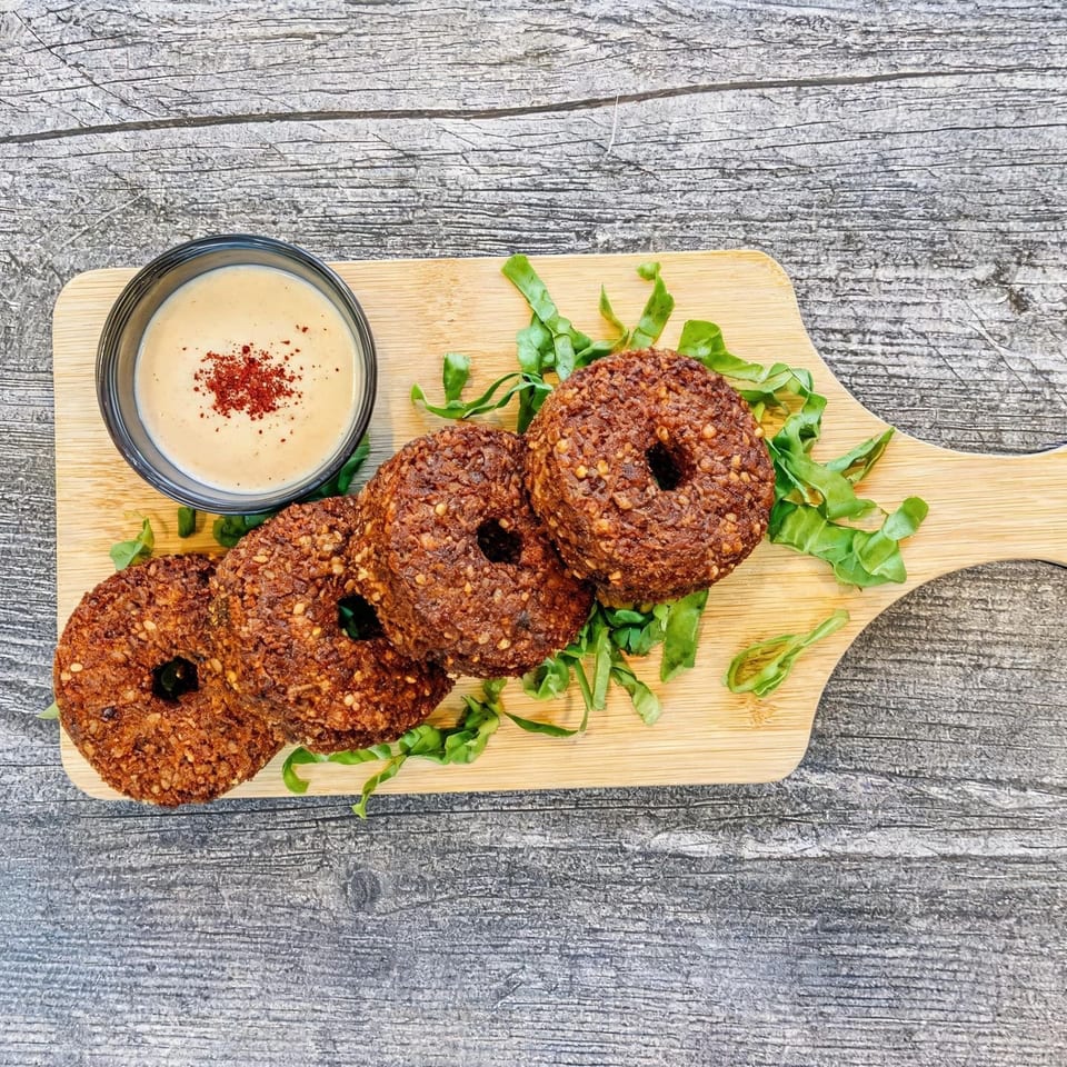 Four crispy falafel patties served with tahini sauce and leafy greens on a wooden serving board.