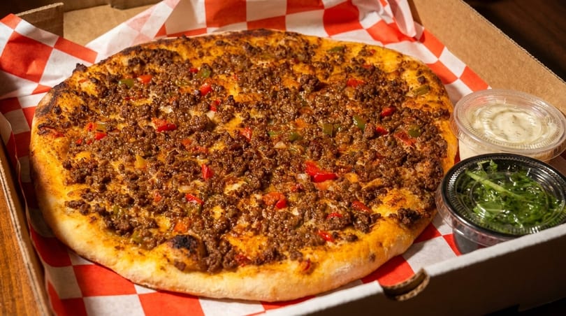 A round pizza topped with ground meat, red and green peppers, and onions in a box.