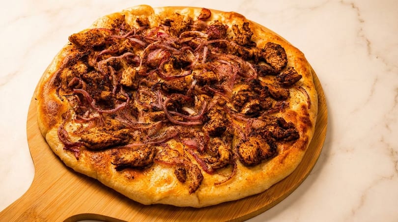 A chicken and red onion pizza on a wooden peel, against a marble background.