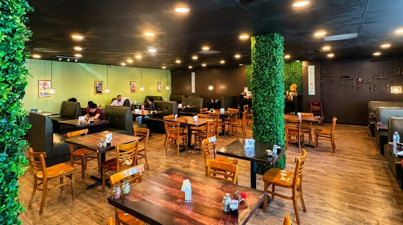 A restaurant interior with wooden tables and chairs, green booth seating, and customers dining.